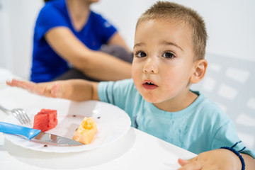 Little boy eating watermelon by the table at home