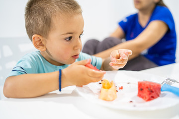 Little boy eating watermelon by the table at home