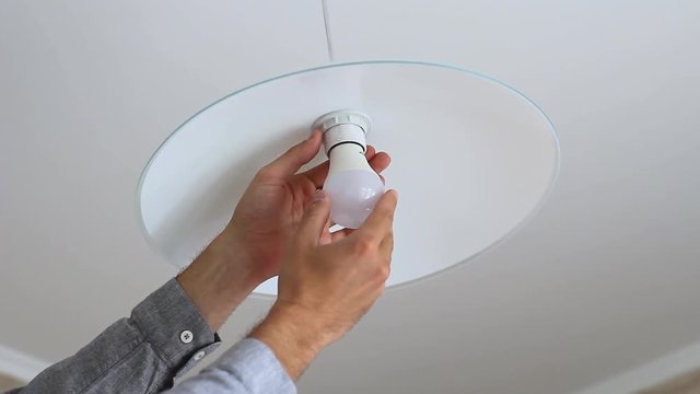 a man's hand is screwing an light bulb into a chandelier in the kitchen