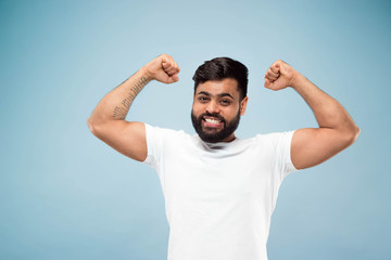 Naklejka premium Half-length close up portrait of young hindoo man in white shirt on blue background. Human emotions, facial expression, ad concept. Negative space. Celebrating, winning, crazy happy.