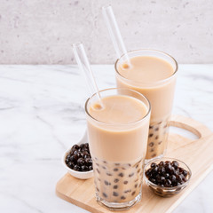 Tapioca pearl ball bubble milk tea, popular Taiwan drink, in drinking glass with straw on marble white table and wooden tray, close up, copy space.