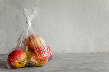 Fresh natural fruit in plastic bag on grey background. The concept of harm of food storage in artificial packages.
