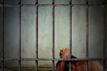 Alone male prisoner in the jail cell is not wear a shirt while holding his head and the body has stains and bruises