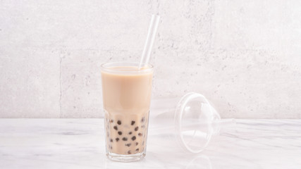 Tapioca pearl ball bubble milk tea, popular Taiwan drink, in drinking glass with straw on marble white table and wooden tray, close up, copy space.