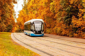 Modern tram on the background of autumn foliage. Rail ecological city transport on the background...
