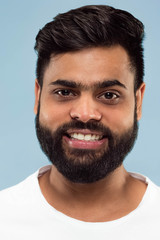 Close up portrait of young hindoo man with beard in white shirt isolated on blue background. Human emotions, facial expression, ad concept. Negative space. Standing and smiling.