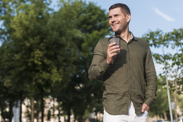 Naklejka na ściany i meble Smiling man standing in park holding disposable coffee cup