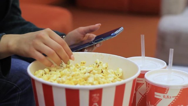 Female hand takes popcorn from box and uses mobile device