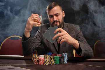 Handsome bearded man is playing poker sitting at the table in casino.