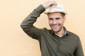 Man standing over beige background holding hat and smiling