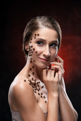 Beautiful smiling girl with naked shoulders touches her face with her hands. Coffee beans were...