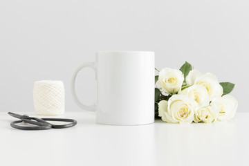 Mug mockup with a bouquet of roses and workspace accessories on a white table.