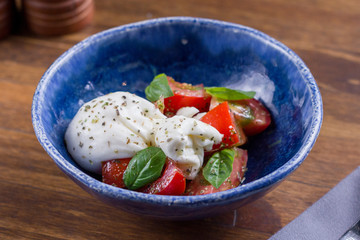 Salad with Italian white burrata cheese served with tomatoes and pesto on blue plate on wooden background. Healthy, tasty, food. Diet, holidays, recipe concept. Free space for text. Selective focus