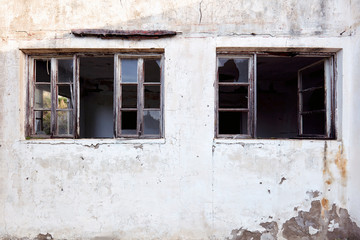Exterior of an old abandoned cottage with broken wooden window frames and white cracked wall