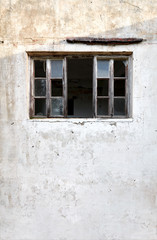 Exterior of an old abandoned cottage with broken wooden window frames and white cracked wall