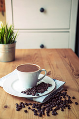Cup of coffee and roasted beans on wooden table, close up
