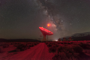 Dirt road leading towards a large radio dish with the Milky Way Galaxy behind it