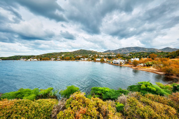 Obraz premium Moody view of Gumusluk bay and village in Bodrum, Mugla, Turkey on a cloudy winter day. Beautiful calm sea, sky and meadow landscape.
