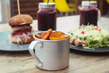 French fries in mug with meat burger and caesar salad. Fast food cafe