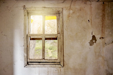 Fototapeta premium Interior of a ruined house with old, dirty and cracked white wall and a broken window frame with a green meadow field view