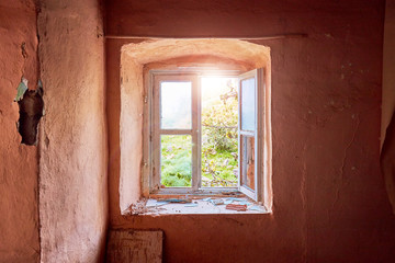 Interior of a ruined old cottage with a light pink wall and a broken wooden window frame viewing a rural green meadow field landscape
