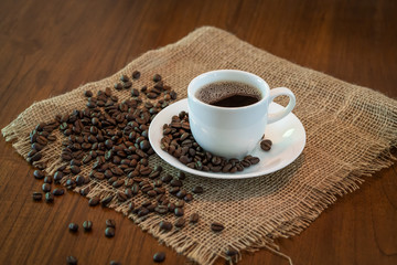 Hot coffee cup with roasted coffee beans on sack and wood table