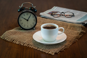 Hot coffee cup and vintage clock newspaper glasses on wood table