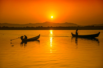 Fisherman on wooden boats casting net for fish on sunset in Asia