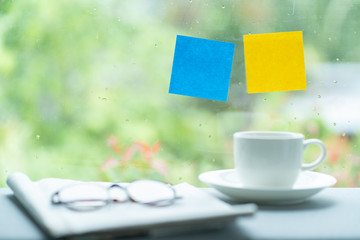 Blue and yellow post it stick on windows with blurred image of coffee cup and glasses