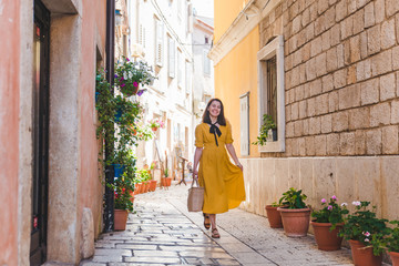 Obraz na płótnie Canvas tourist woman in yellow sundress walking by small croatian city street