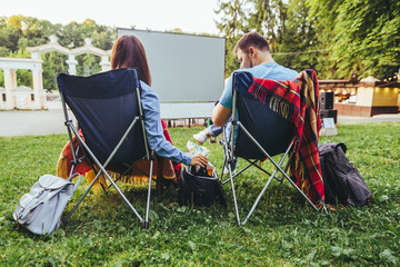 couple sitting in camp-chairs in city park looking movie outdoors at open air cinema