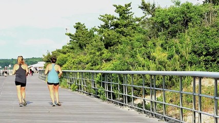 A women takes a selfie of herself while running on a boardwalk with a friend.