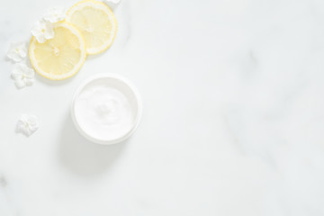 White moisturizing cream with lemon citrus and flower petals on marble background. Skin care beauty treatment with jar of body moisturizer. Bio organic, natur
