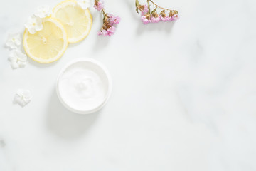 Obraz na płótnie Canvas White moisturizing cream with lemon citrus and flower petals on marble background. Skin care beauty treatment with jar of body moisturizer. Bio organic, natur