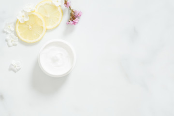 Obraz na płótnie Canvas White moisturizing cream with lemon citrus and flower petals on marble background. Skin care beauty treatment with jar of body moisturizer. Bio organic, natural beauty products concept.
