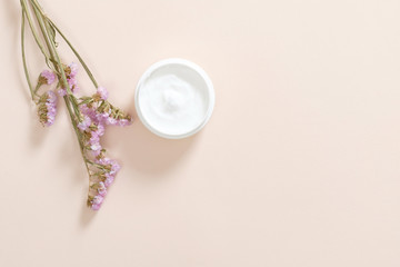Fototapeta na wymiar Jar with moisturizing body cream and dry flower on pastel pink background. Skin care cosmetic, anti aging concept. Minimal flat lay style composition, top view, copy space.