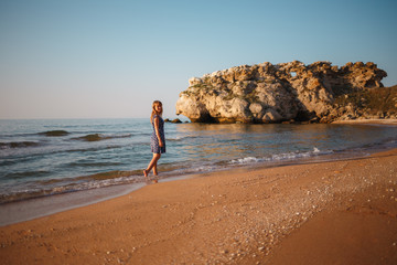 Beautiful girl in a dress walks along the sea sandy shore at sunset