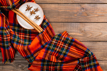 Flatlay autumn composition. Red women fashion scarf and cinnamon stick on plate on wooden background. Flat lay, top view, overhead. Cozy home desk, hygge, autumn fall concept