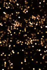 Blurry golden and white fairy lights in dark night creating beautiful bokeh effect with glowing...