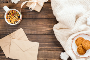 Autumn composition. Cup of herbal tea, women fashion white sweater, craft paper envelope, gift, cotton on wooden background. Flat lay, top view, overhead. Cozy home desk, hygge, autumn fall concept