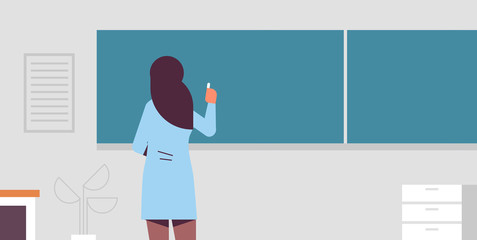 arab female school teacher standing in front of green chalk board rear view woman in traditional clothes writing on chalkboard education concept modern classroom interior flat portrait horizontal