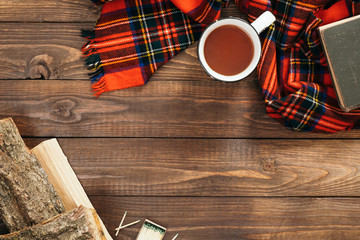 Flatlay composition with red scarf, cup of tea, firewood, book on wooden desk table. Hygge style, cozy autumn or winter holiday concept. Flat lay, top view, overhead.