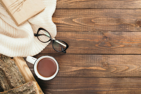 Flatlay composition with white knitted scarf, cup of tea, woman glasses, firewood on wooden desk table. Hygge style, cozy autumn or winter holiday concept. Flat lay, top view, overhead.