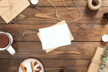 Autumn flatlay composition with letter, blank paper card, cup of tea, gift box, cinnamon sticks, envelope, rope, candles on wooden background. Cozy autumn or winter holiday concept. Flat lay, top view