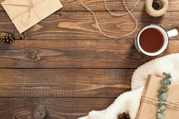 Autumn flatlay composition. Frame made of craft paper envelope, cup of tea, rope, gift box, white knitted scarf on wooden background. Autumn hygge style desk table or winter holiday concept.