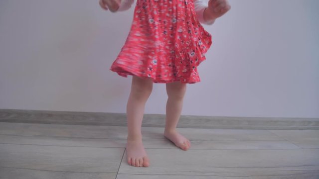A little blond girl with a red dress is spinning and dancing
