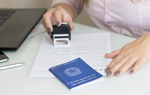 A portfolio of Brazilian workers (Translation "Work Permit, Ministry of Labor and Social Security Brazil CTPS"), female hand signing a work contract background.