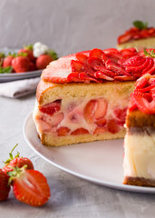 Cut biscuit cake with strawberries and vanilla jelly decorated with strawberry slices and mint leaves on a gray background. Fraisier cake .Vertical orientation, side view, Close-up.