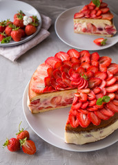 Cut biscuit cake with strawberries and vanilla jelly decorated with strawberry slices and mint leaves on a gray background. Fraisier cake .Vertical orientation, side view.