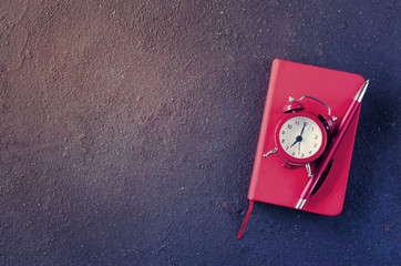 Alarm clock, notepad and pen on dark background. Concept time management or education.